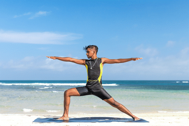 A photo of a man in a yoga pose on a white sand beach with the clear blue waters and blue sky behind him; he represents a nimble restaurant owner who's ready to change menu prices as the price of high-cost, volatile items
