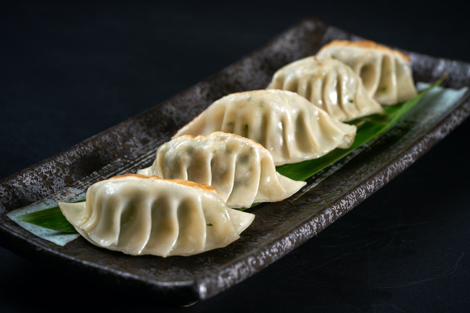 Four dumplings resting on a bamboo leaf and beautifully laid out on a rectangular plate, illustrating how restaurants could promote National Dumpling Day, just one of more than 800 food holidays throughout the year.