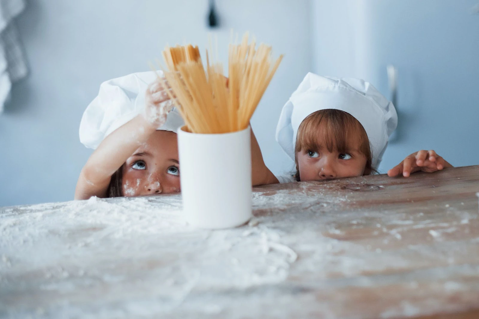 Two children wearing chefs' hats in front of a flour-dusted counter