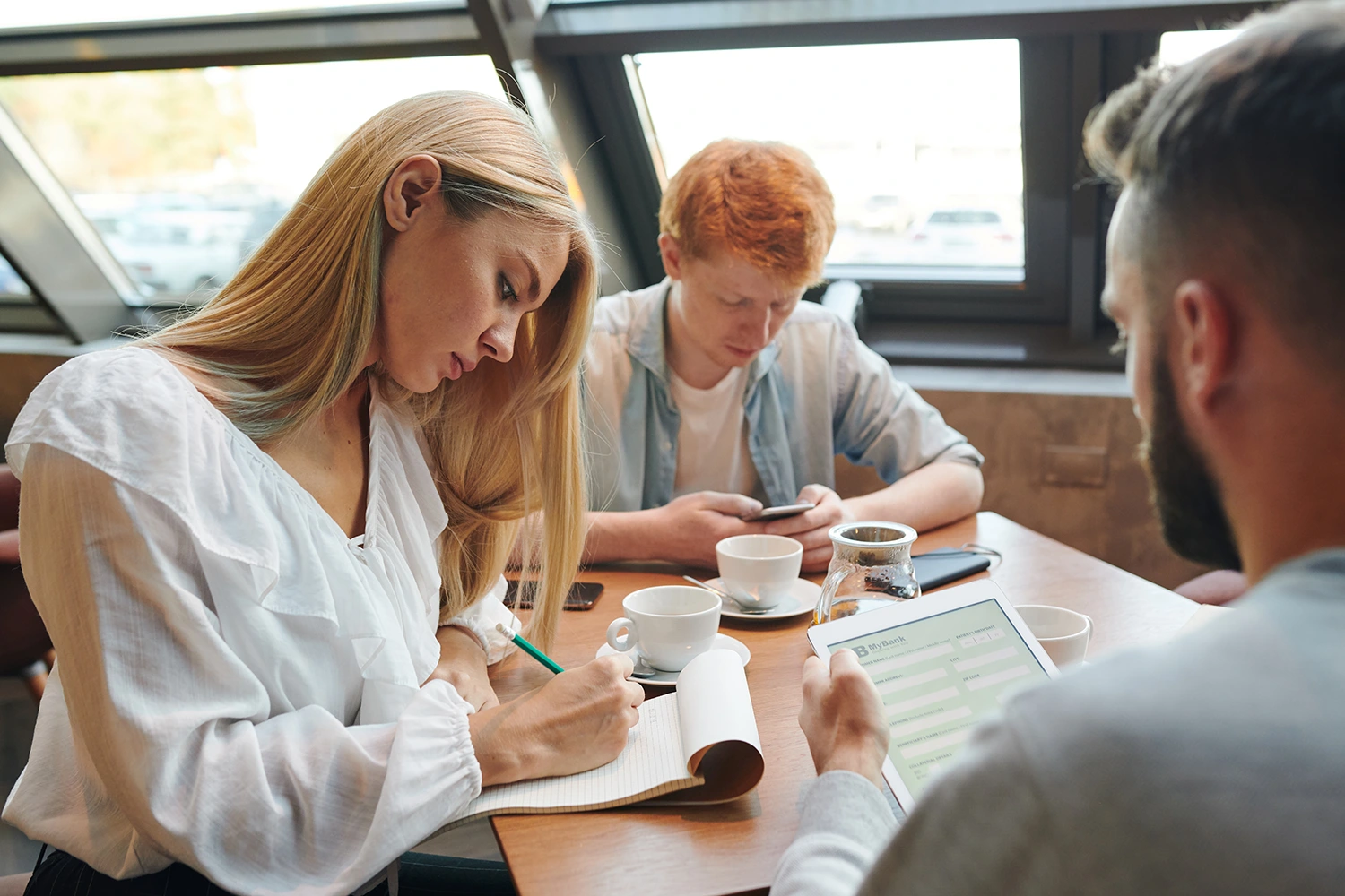 A CRM for your restaurant should be a top priority. In this image, two men and a woman sit at a restaurant table, each engaged in their own pursuits.