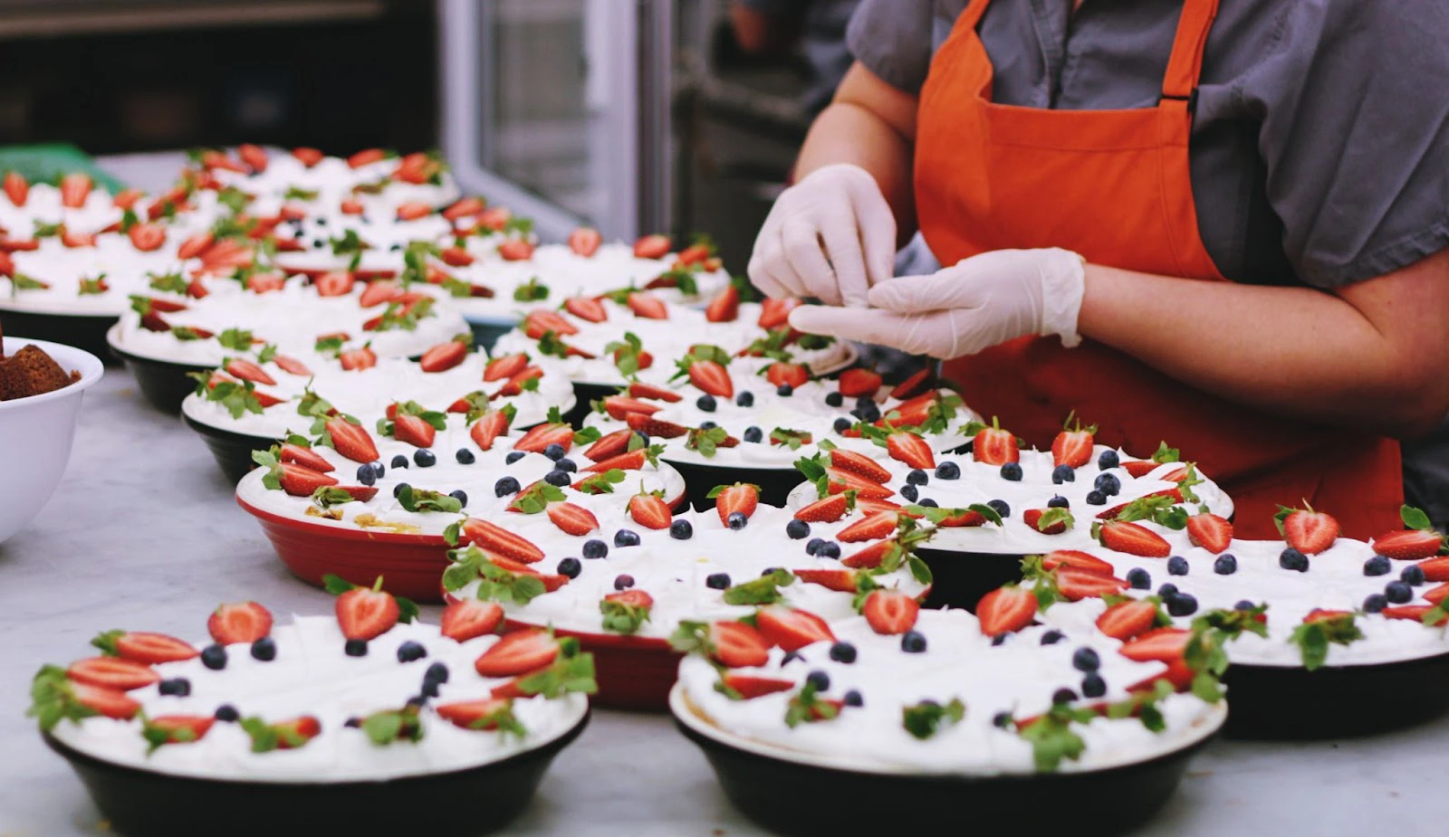 Pastry chef preparing dishes with whipped cream, strawberries, and blueberries