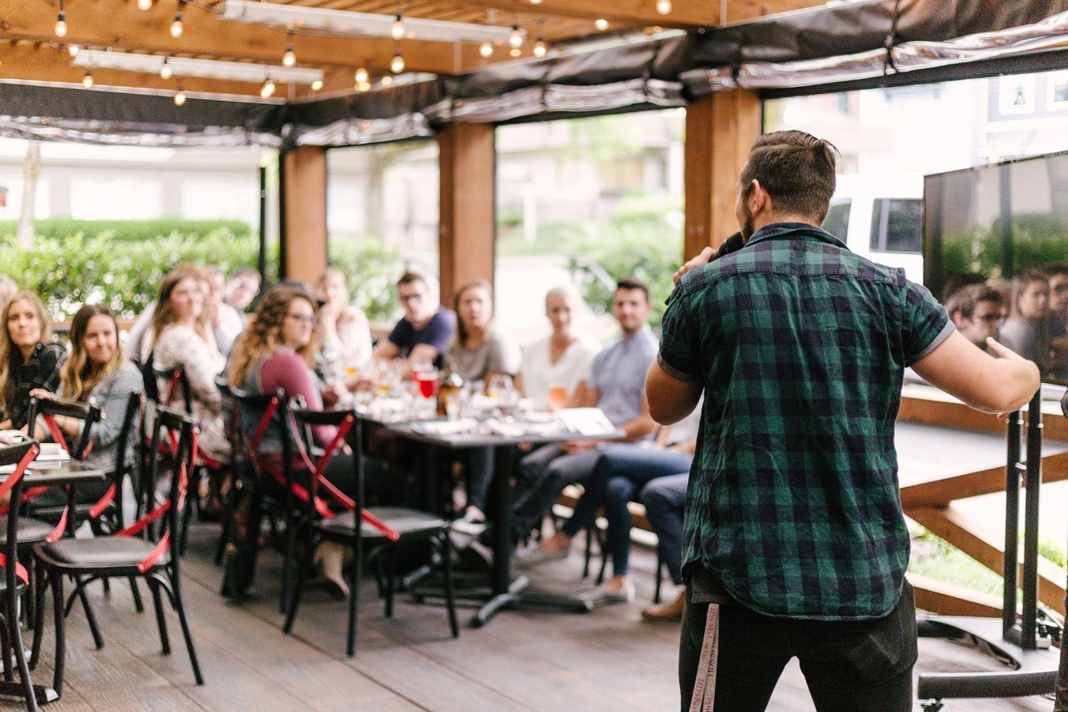 A man speaking to a group of outdoor diners, possibly representing a restaurant owner speaking with influencers and loyal diners about his new seasonal menu.