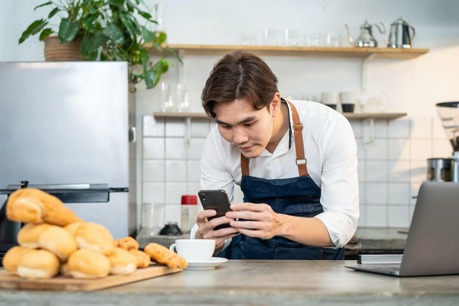 A man in an apron, showcasing his culinary creativity, is seen looking at his phone in a kitchen.