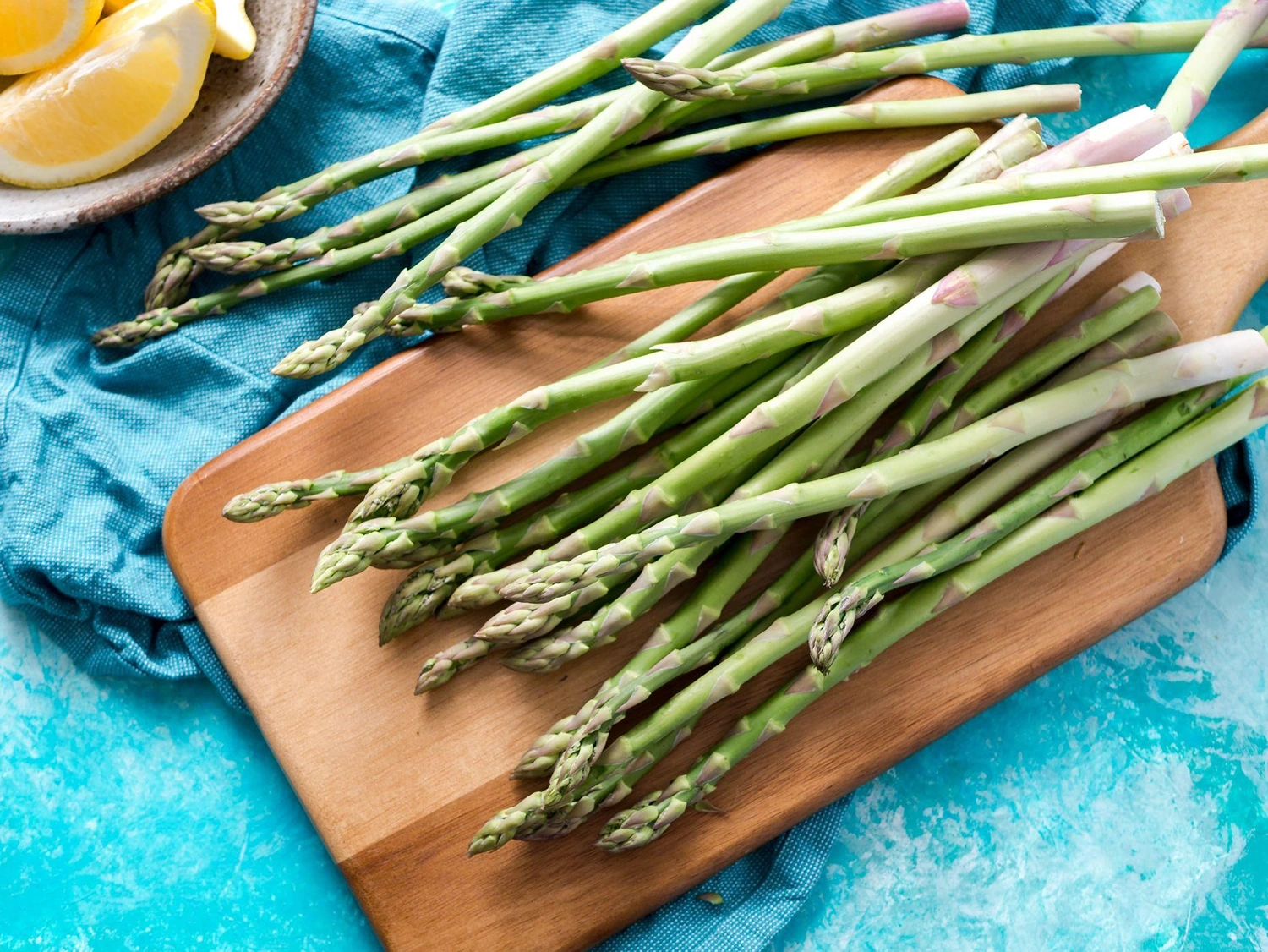 Fresh asparagus on a cutting board with lemon slices, perfect for a seasonal menu.