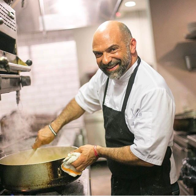 The resilient Chef Rocco Carulli succeeds in the restaurant industry, smiling while cooking in a kitchen.