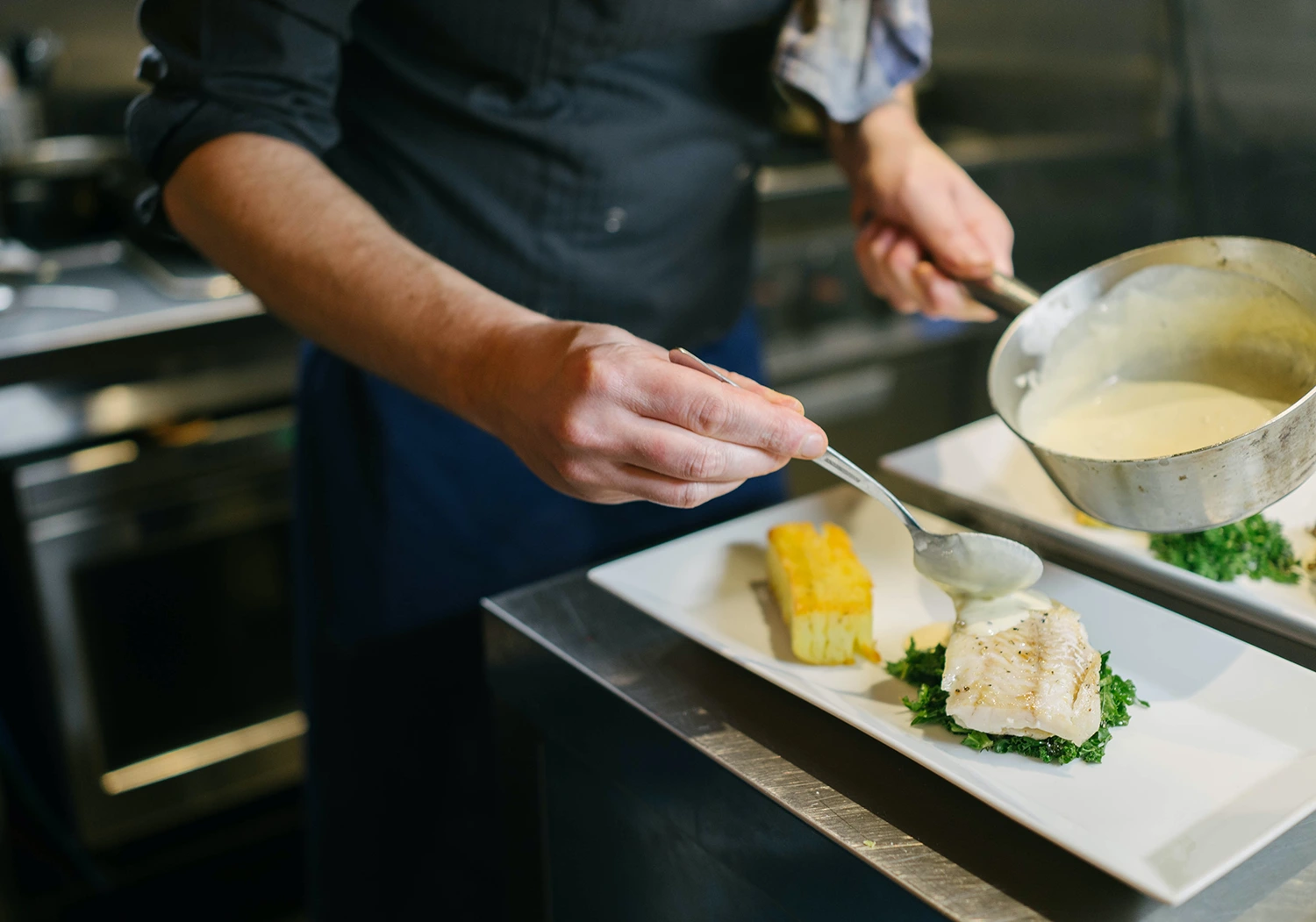 Chef pouring sauce on a plate of food to increase restaurant loyalty.