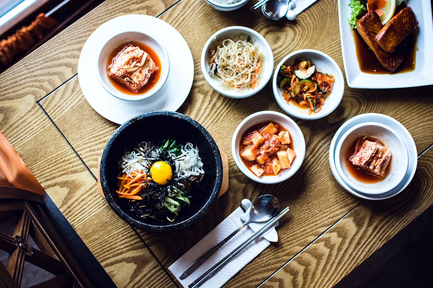 Plates and bowls filled with Korean food on a wooden table.