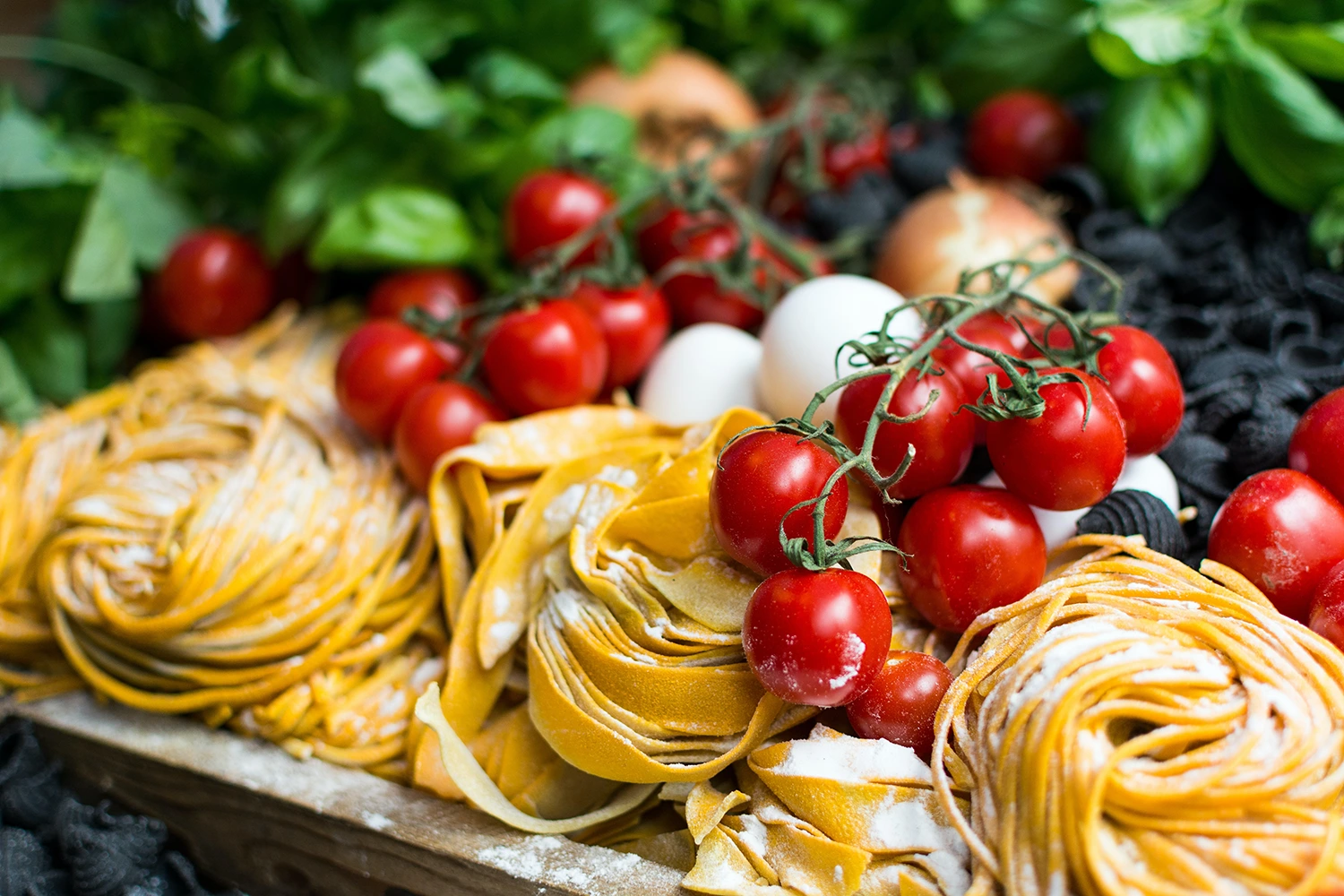 A visually appealing wooden tray filled with pasta, tomatoes, and olives to entice customers through a profitable email newsletter.