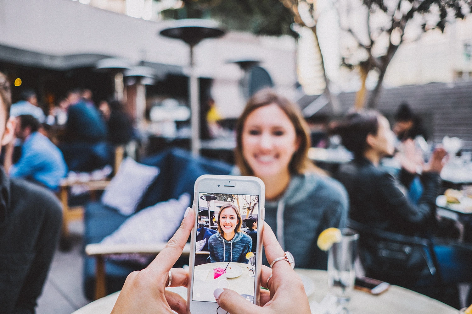 Someone holding a phone and capturing a woman's picture at an outdoor eatery; perhaps they visited because of the restaurant's email newsletter.