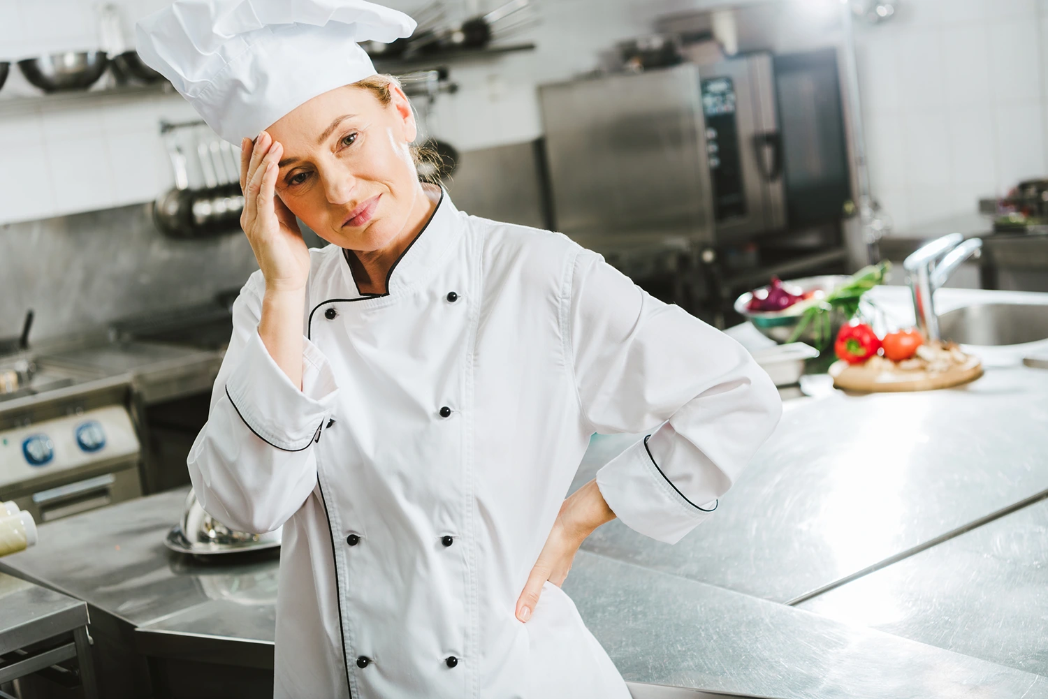 A woman in a chef's uniform is stressed, perhaps because she's diligently monitoring ingredient prices while keeping an eye on restaurant costs.